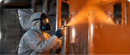 Worker applying protective industrial coating while spraying equipment